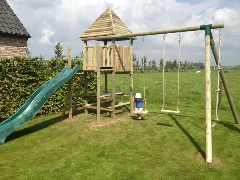 Houten Bullwood-speeltoren met groene glijbaan en schommels in een tuin